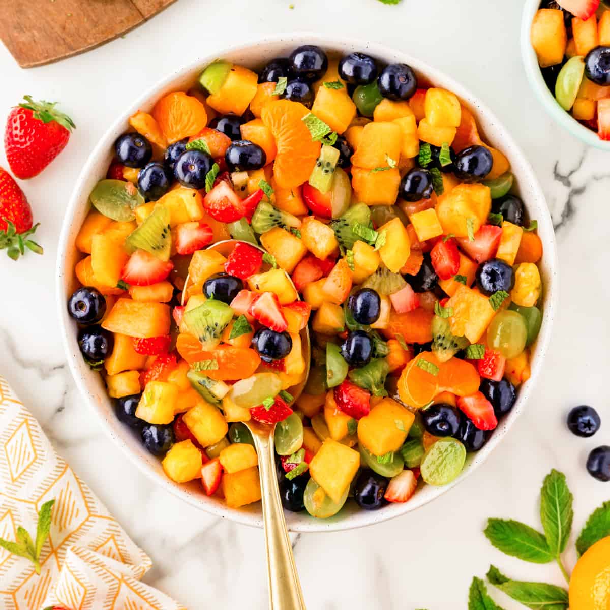Square photo of an overhead shot of fruit salad in a bowl with a spoon.