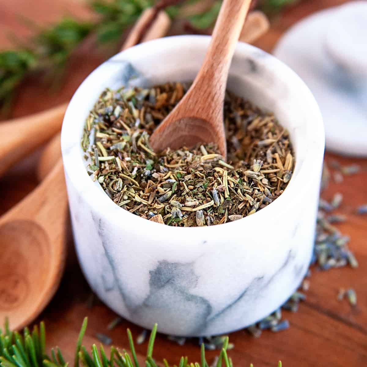 Square photo of herbs de provence in a mortar and pestle bowl with a spoon. 