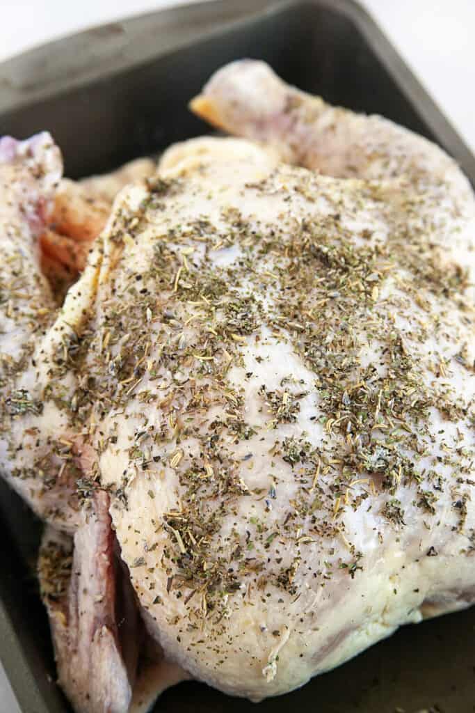 Raw chicken covered in Herbs de Provence in a roasting pan. 