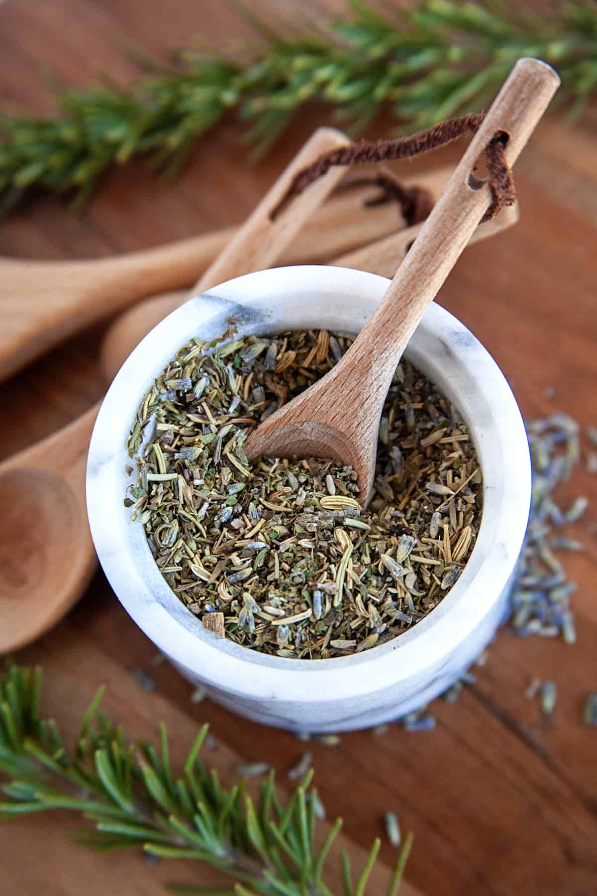 Overhead shot of herbs de Provence in a bowl of a mortar and pestle with a wooden spoon. 