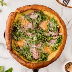 A savory Dutch Baby in a cast iron pan filled with ham, eggs and arugula salad.