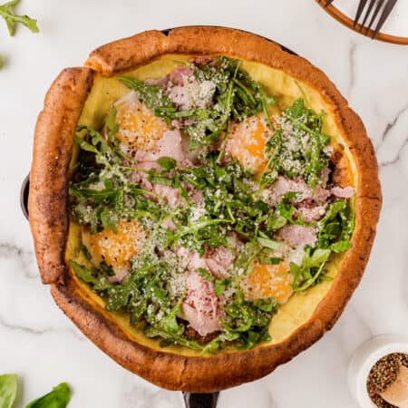 A savory Dutch Baby in a cast iron pan filled with ham, eggs and arugula salad.