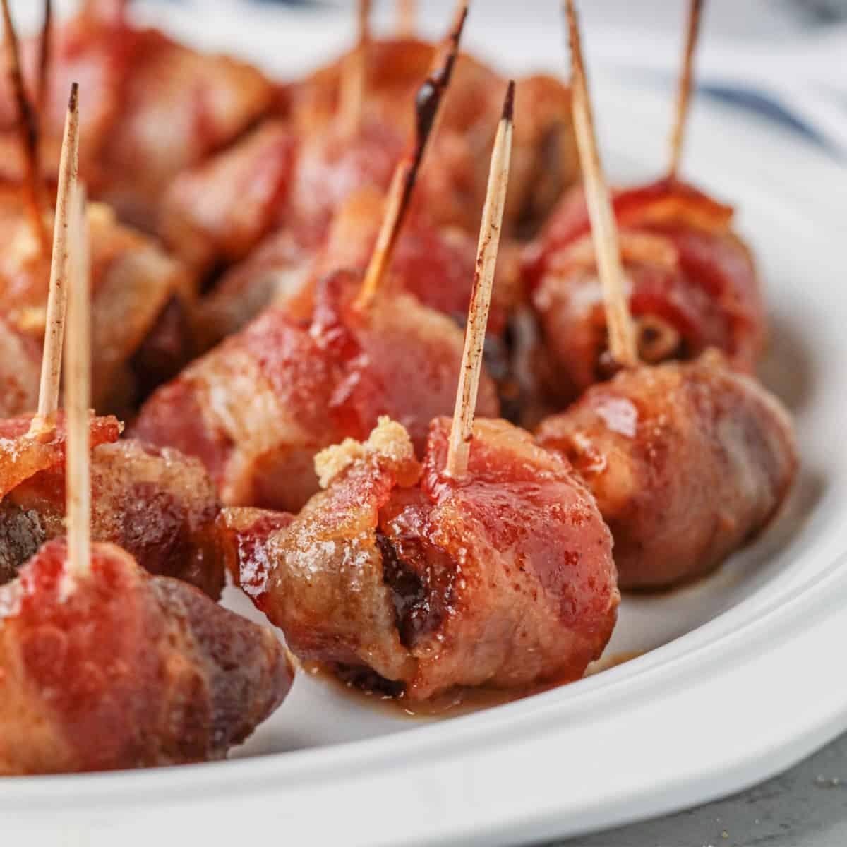 Square photo of bacon-wrapped dates on a white plate. 