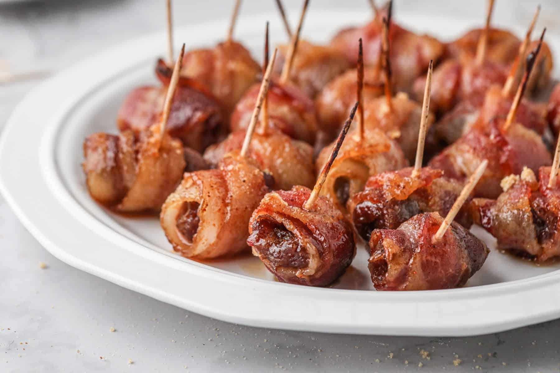Horizontal shot of bacon-wrapped dates on a white plate. 