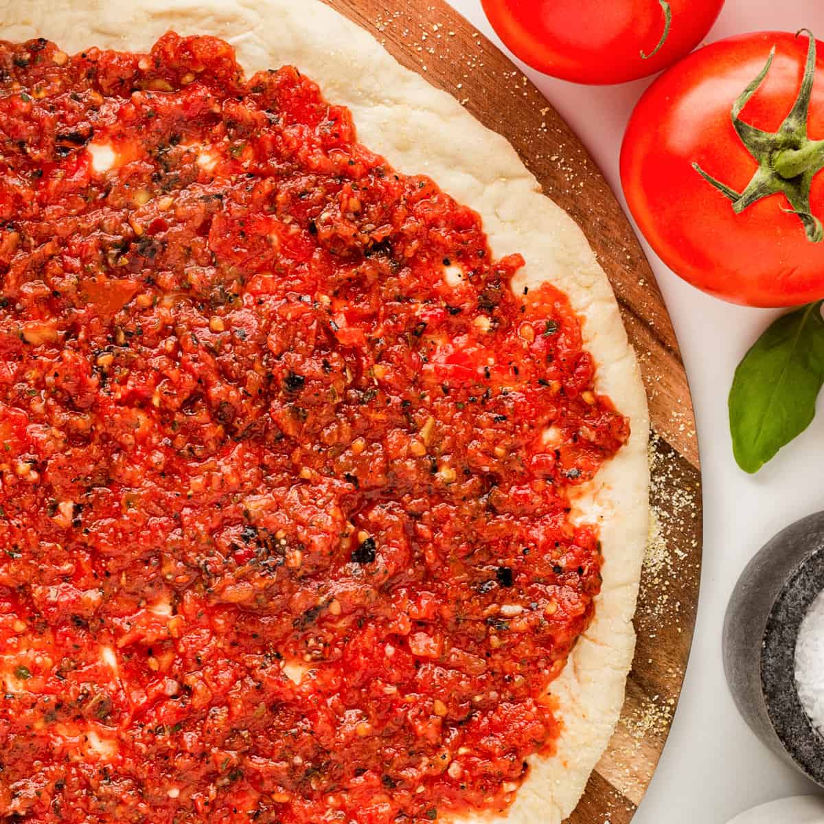 Square overhead shot of pizza sauce on a pizza dough round. 