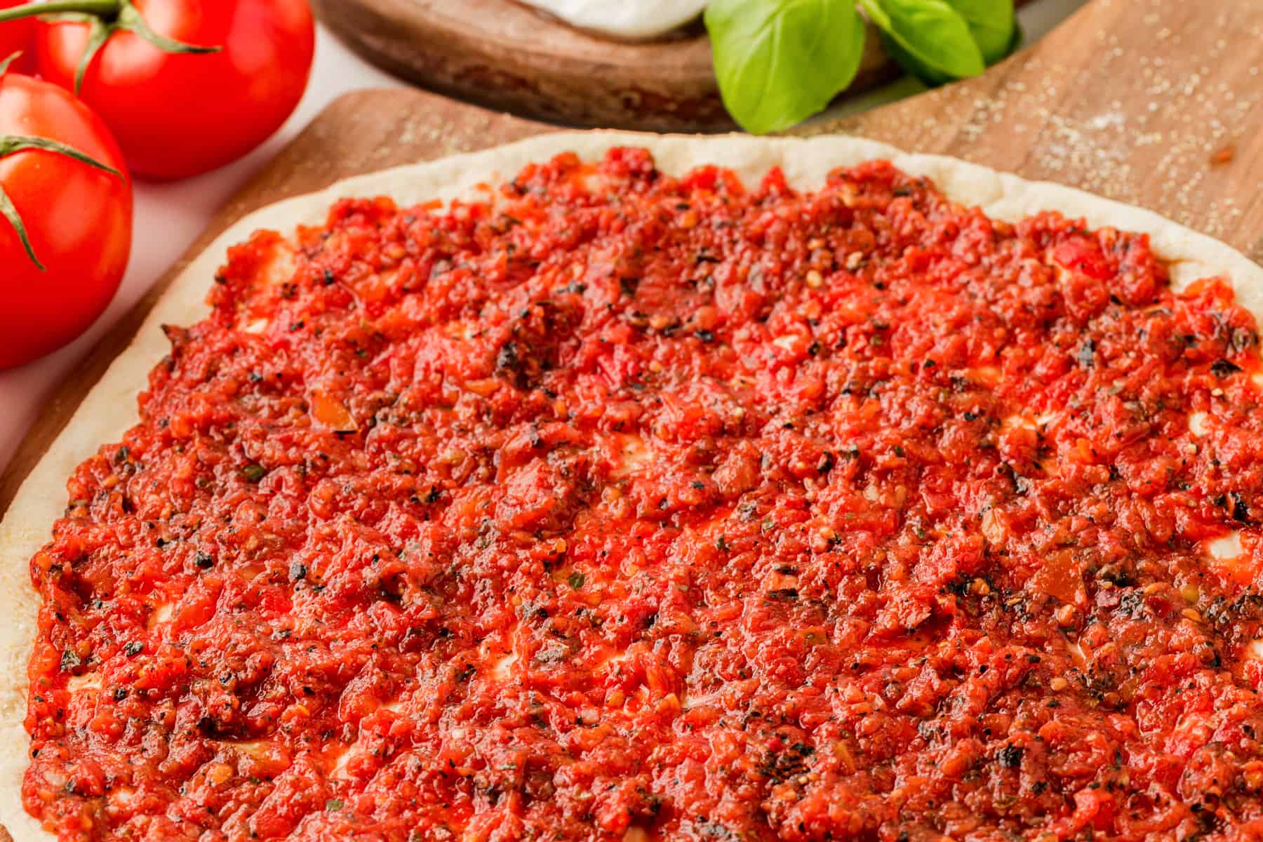 Horizontal photo of pizza sauce on a pizza, unbaked. 