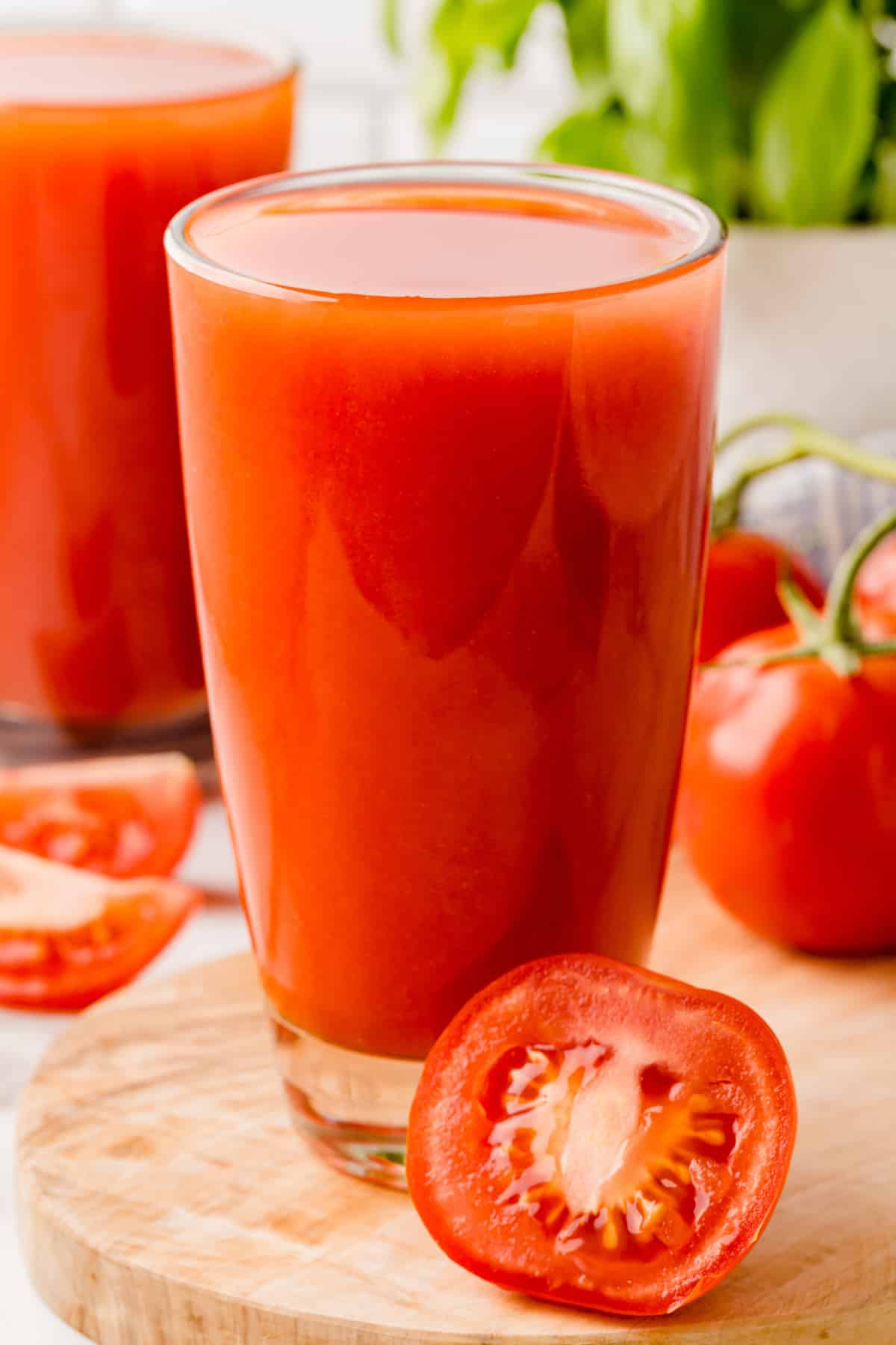 Full glass of tomato juice with a half sliced tomato in front of the glass. 