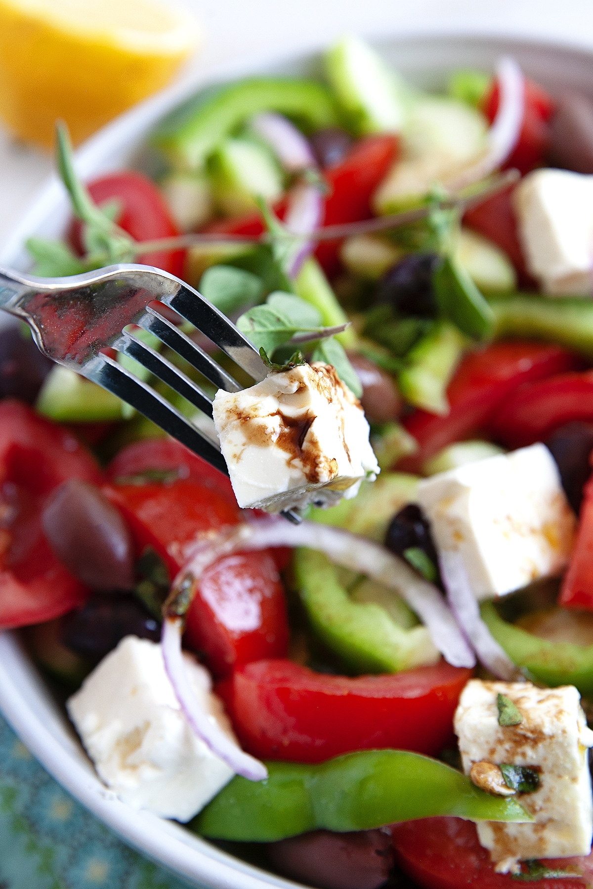 A fork holding a small cube of feta above a Greek salad. 