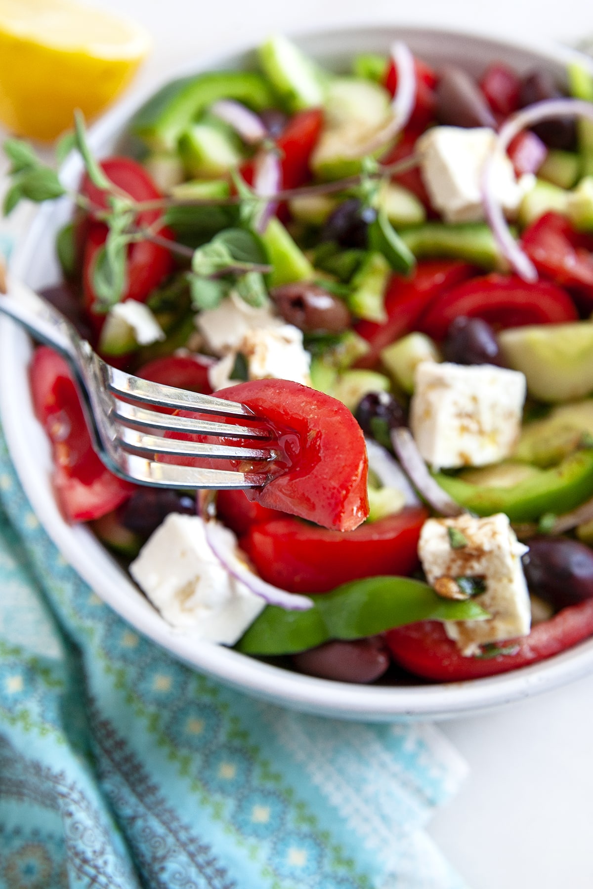 A tomato on a fork above a Greek salad. 