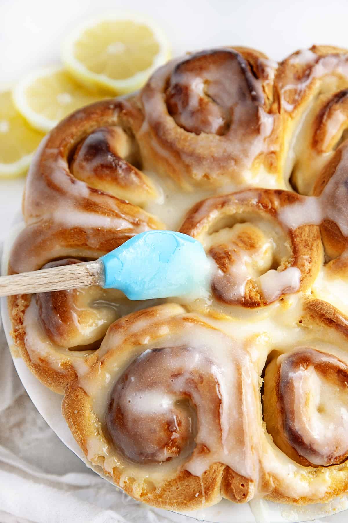  A teal colored spatula spreading on the glaze to the sweet rolls. 