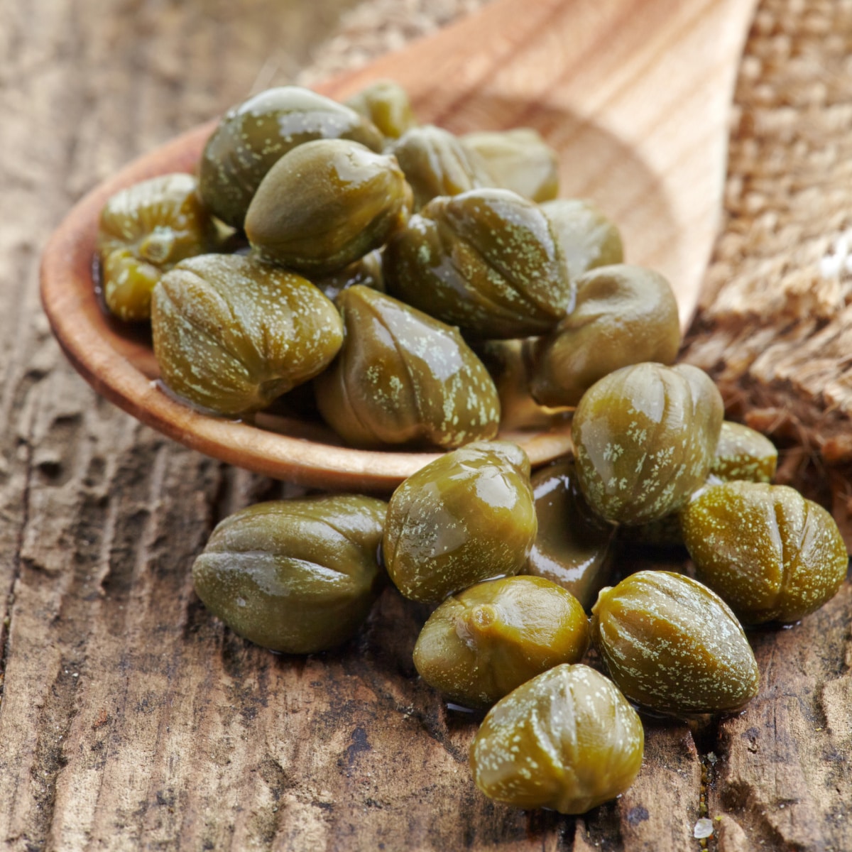 Capers macro in a wooden spoon in a square photo. 