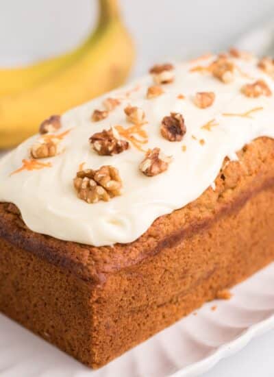 Side view of carrot cake banana bread with frosting and bananas in the background.