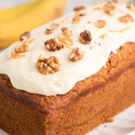 Side view of carrot cake banana bread with frosting and bananas in the background.