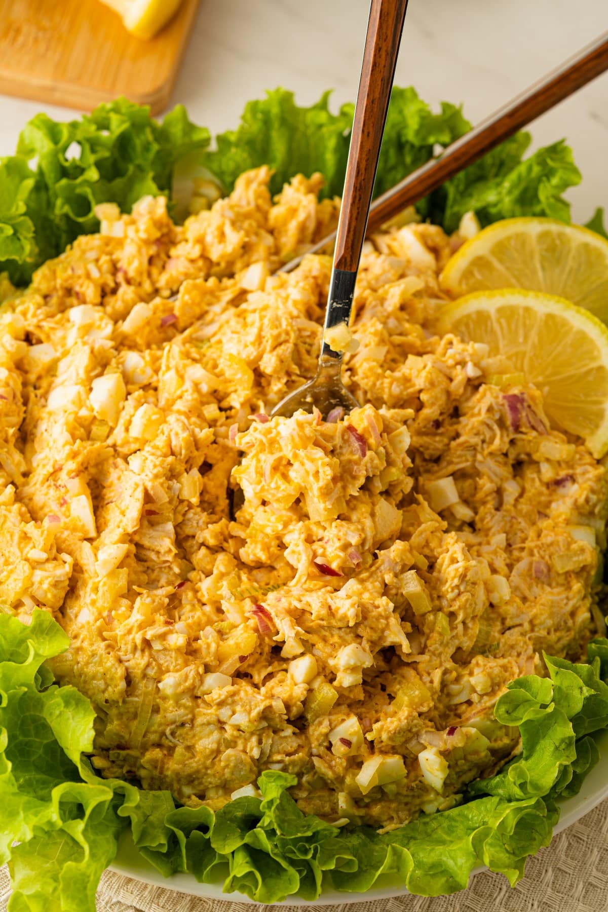 Chicken salad in a bowl with large spoons, lettuce around the edge. 