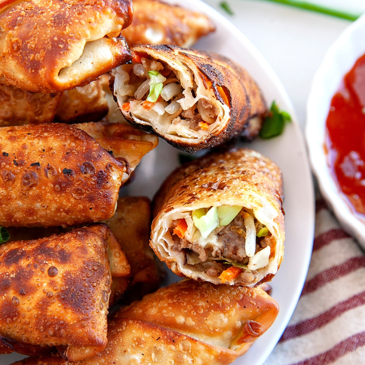 Square photo of crispy homemade egg rolls with one cut in half. 