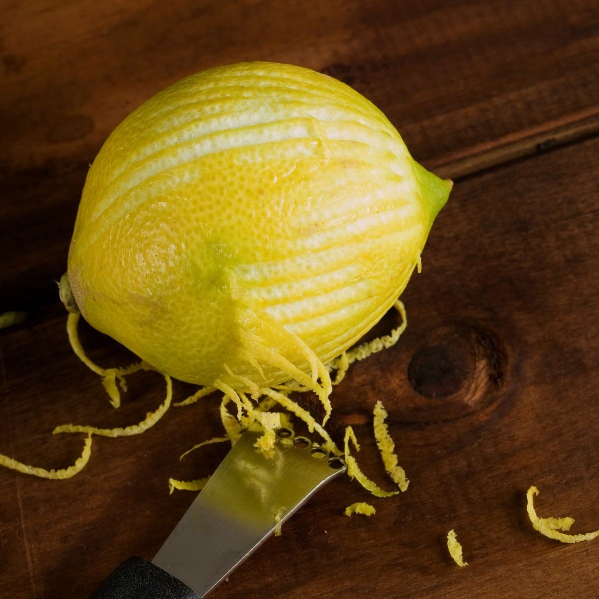 Zesting or zested lemon on wooden table with kitchen implement.