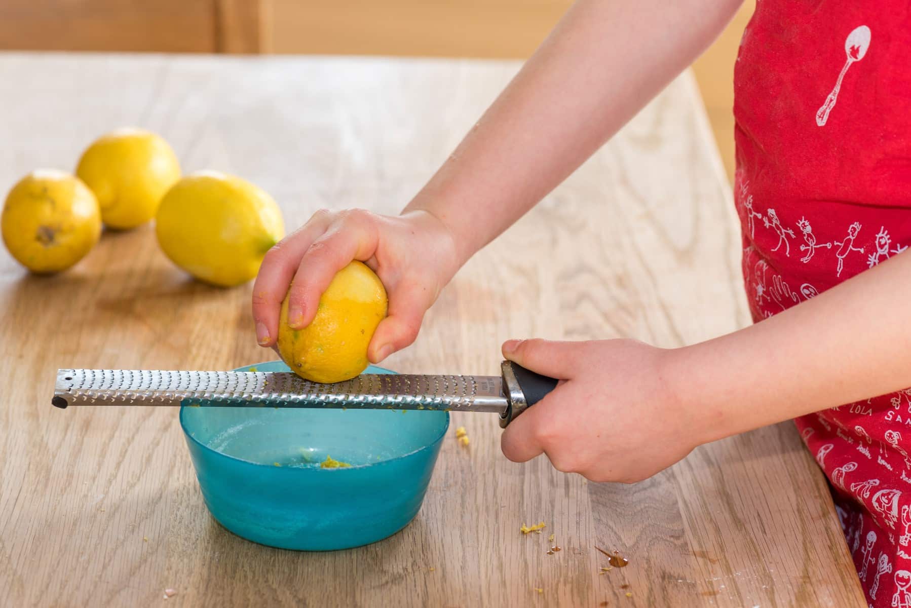 Little girl grating zest of organic lemon on kitchen table.