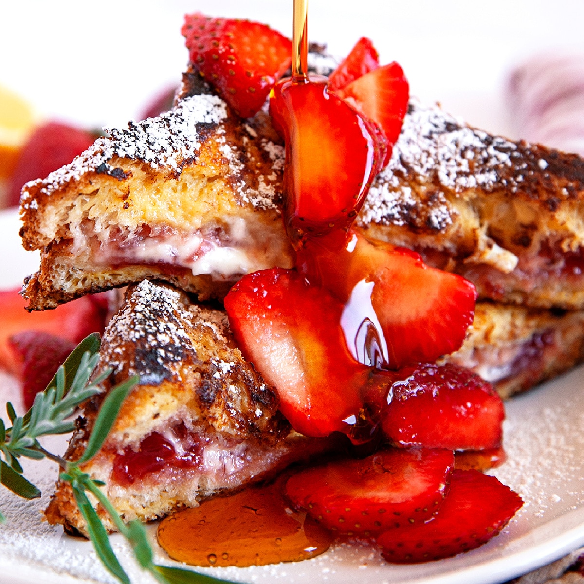 Square photo of maple syrup being poured on strawberry stuffed French toast. 