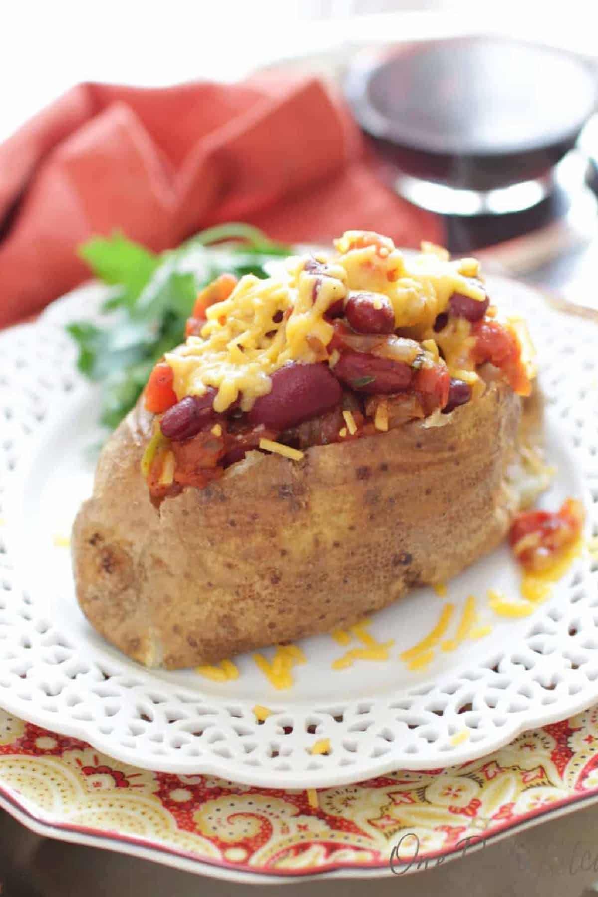 Baked potato with chili and melted cheese on a fancy white plate.