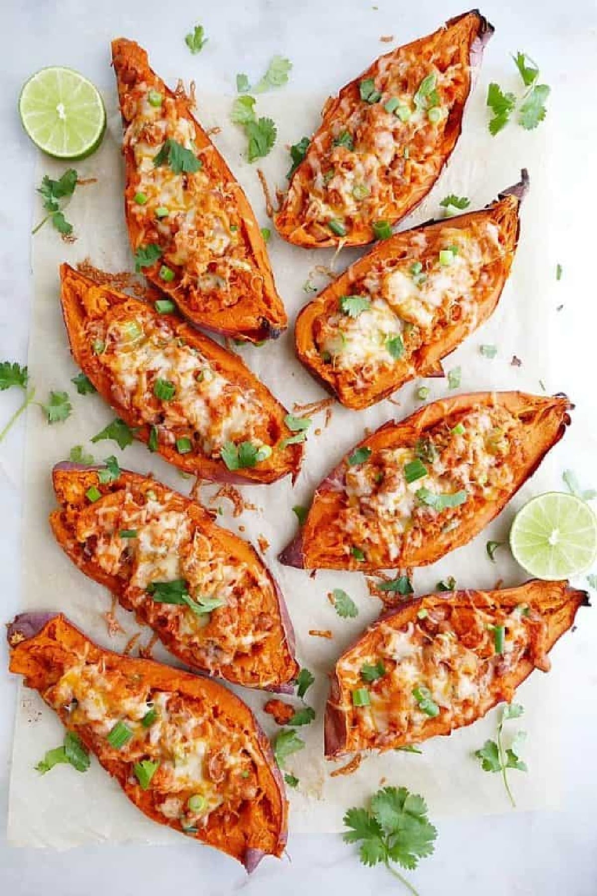 Healthy sweet potato skins with BBQ beans on a white table with with limes slices and cilantro.