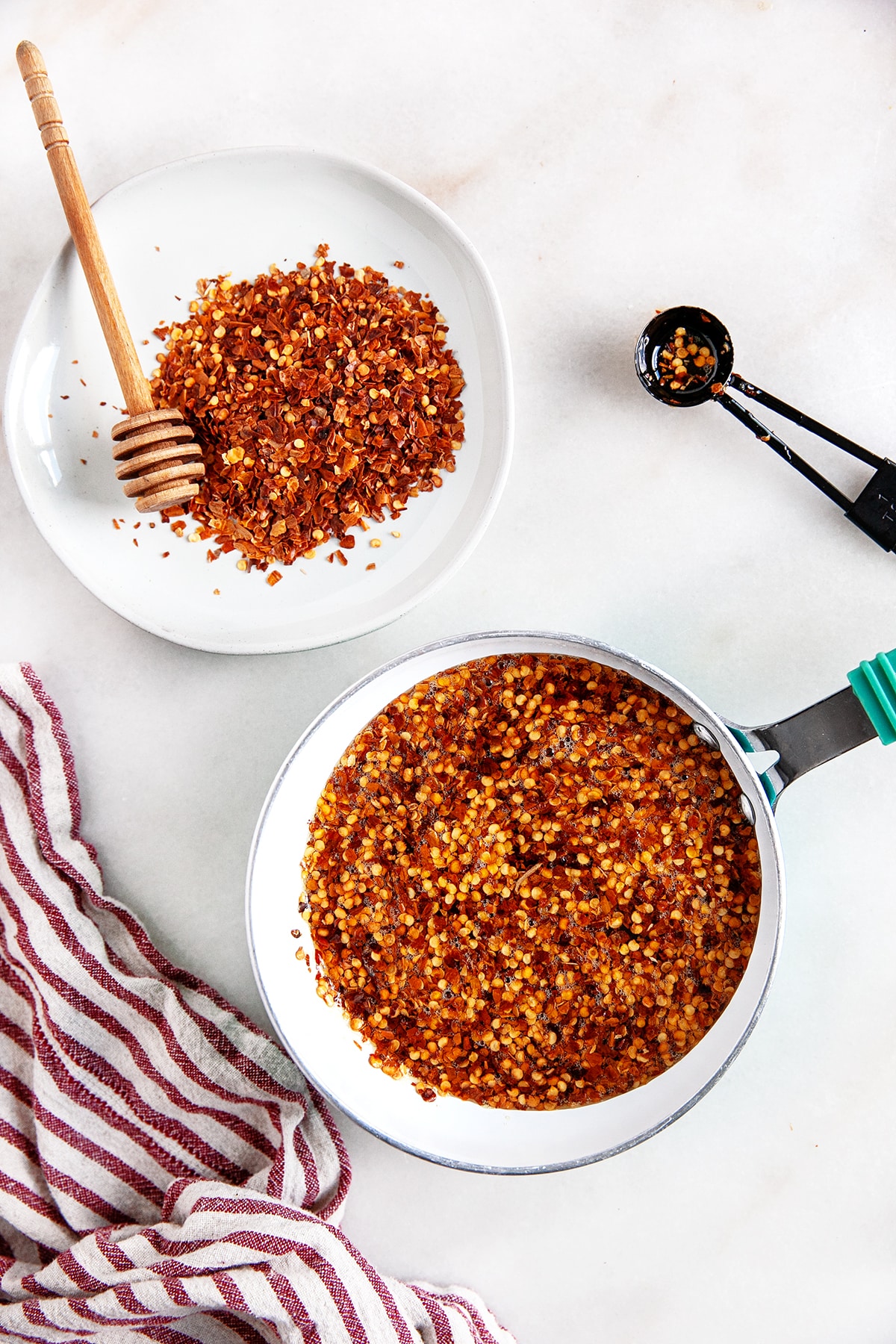 Overhead view of hot honey in a pot with chili flakes and a plate of chili flakes and a measuring spoon. 