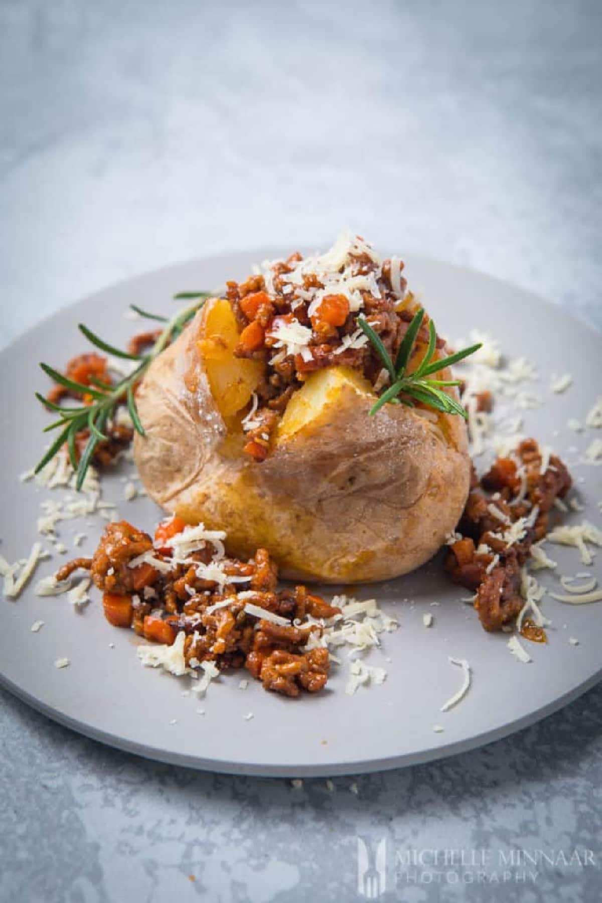 Savoury Mince Fill Baked Jacket Potatoes on a white plate with rosemary garnish.