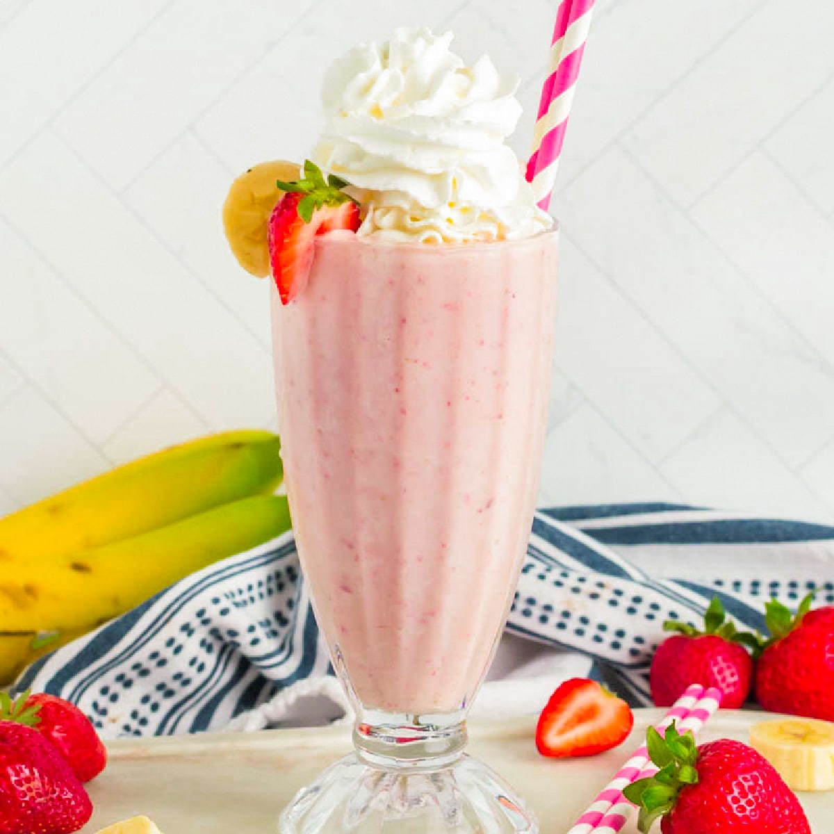 Milkshake in a glass topped with whipped cream and straw. 