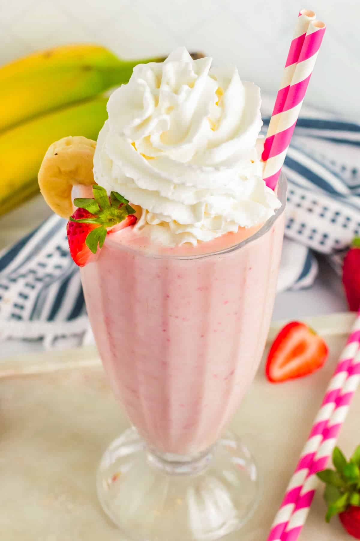 Strawberry Banana Milkshake topped with whipped cream and garnished with a slice of strawberry and a slice of banana. 