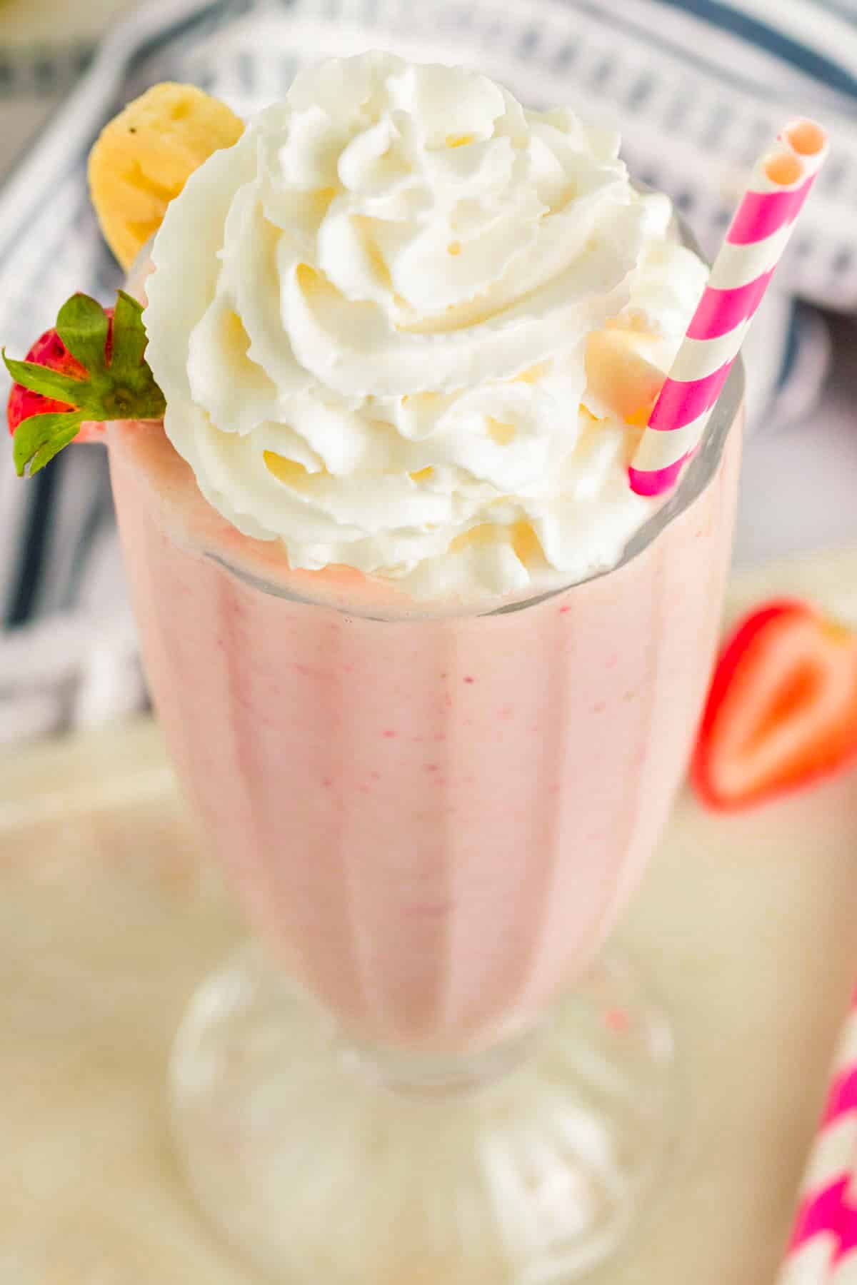 Strawberry Banana Milkshake with whipped cream on top and a striped pink and white straw. 