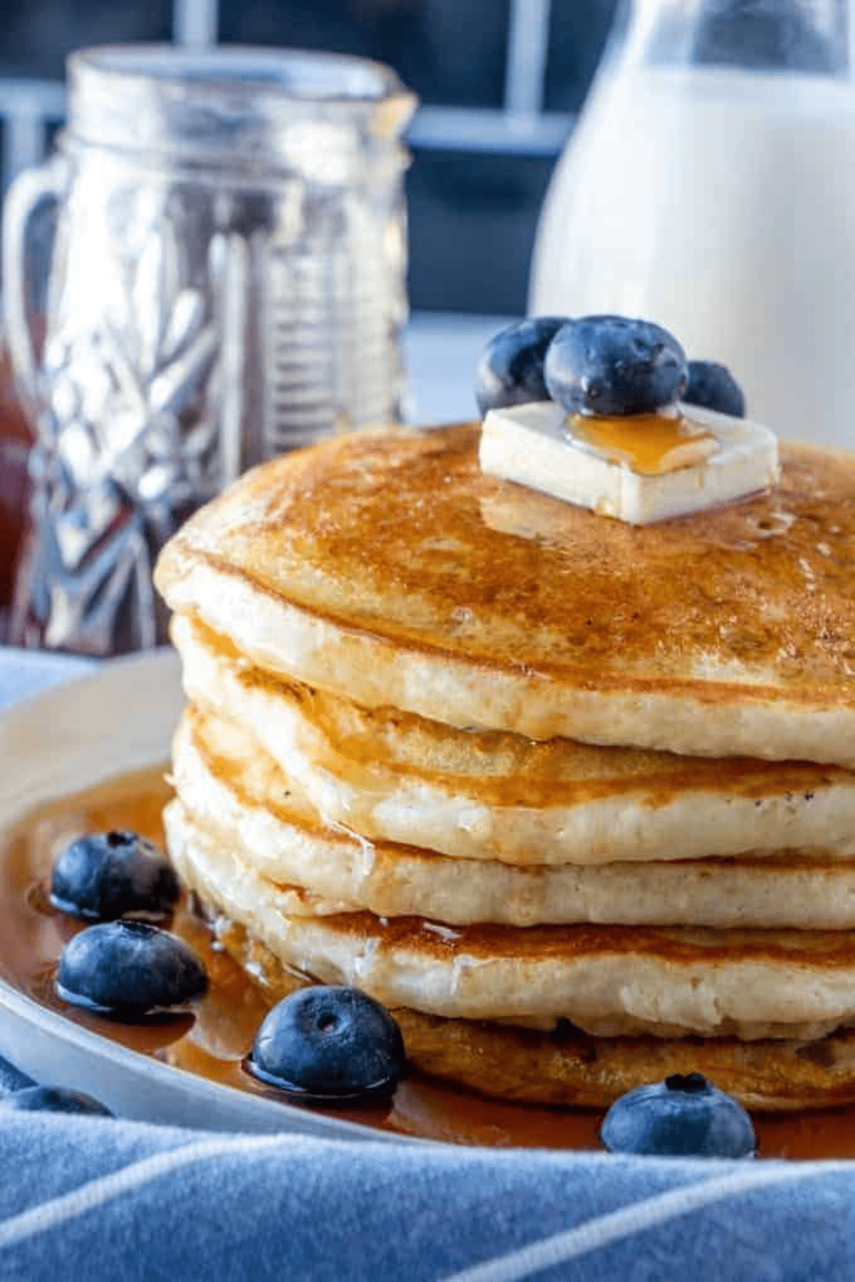 Stack of Buttermilk Blueberry Pancakes with maple syrup, butter and more blueberries. 