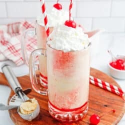 Two cherry floats on a round board with straws, cherries and ice cream scoop around.