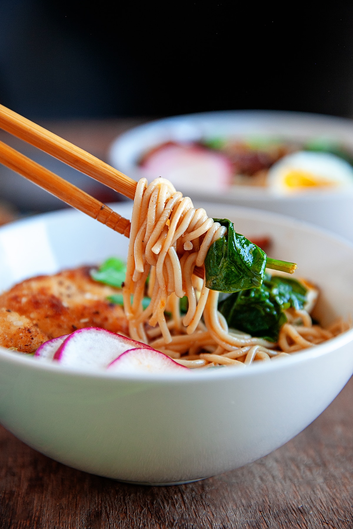 Close-up of ramen noodles and spinach on chopsticks. 