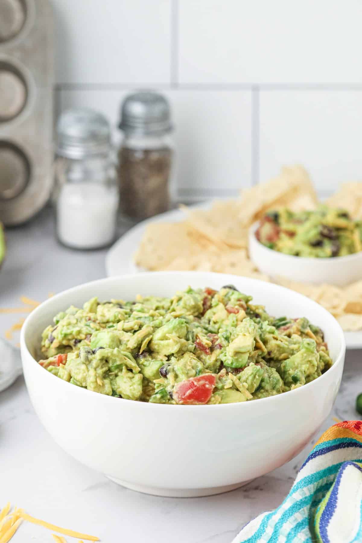 Large bowl of guacamole with chips and guacamole in the background. 