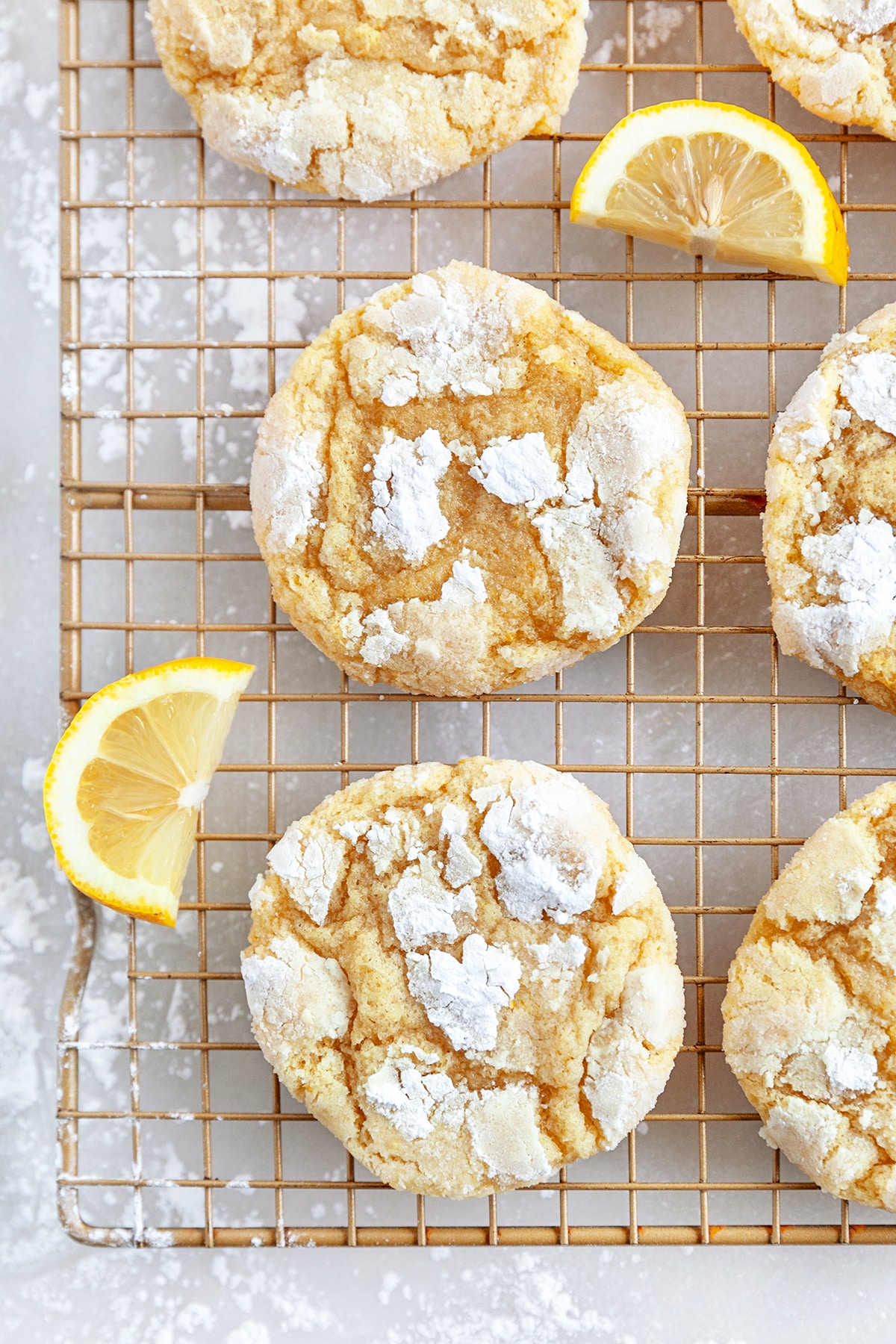 Lemon crinkle cookies on a cooling rack with sliced lemon pieces. 