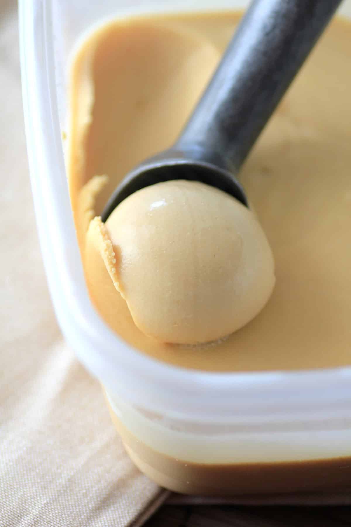 Scooping out salted caramel ice cream from a tub. 
