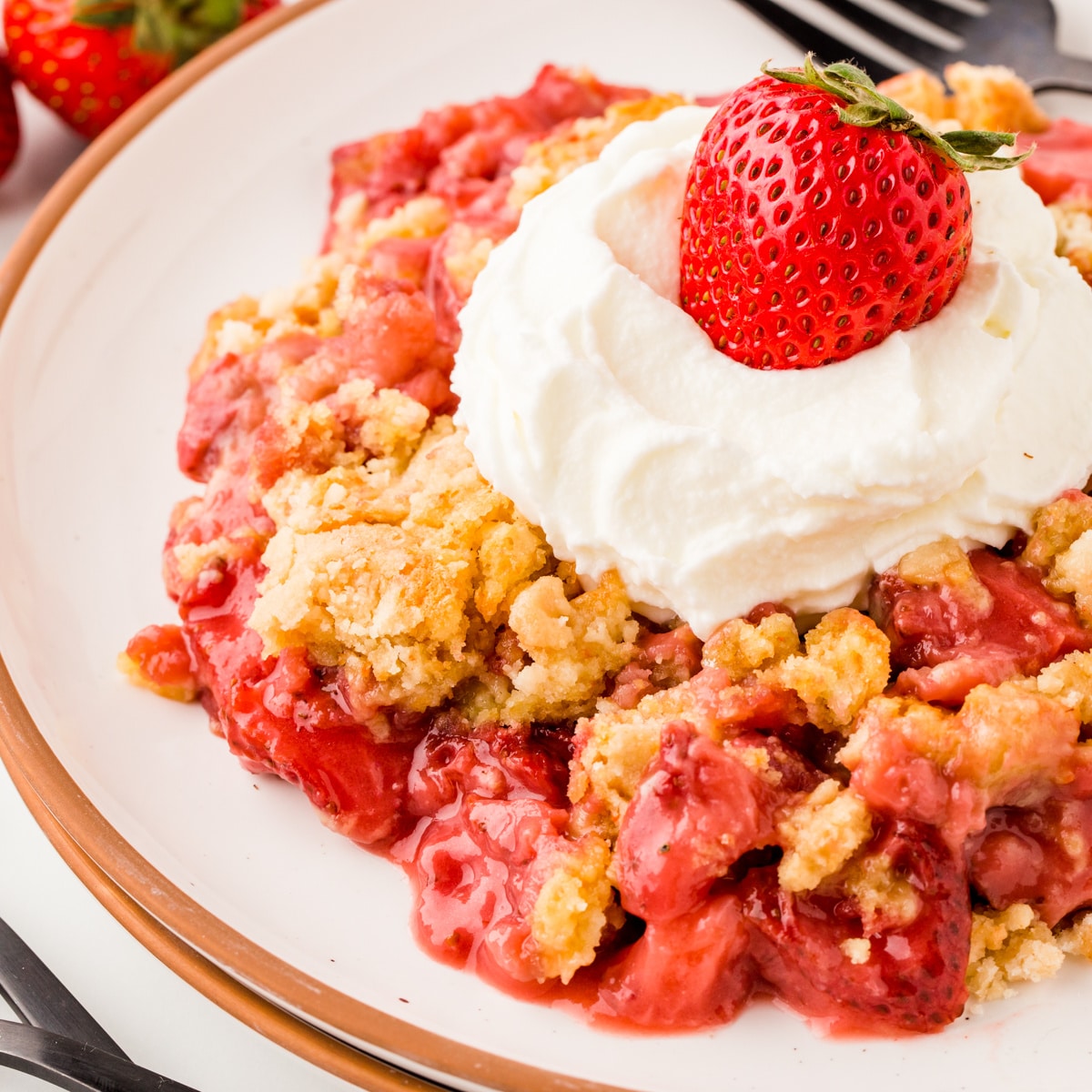 Strawberry Dump Cake on a plate with Whipped Cream and a strawberry on top. 