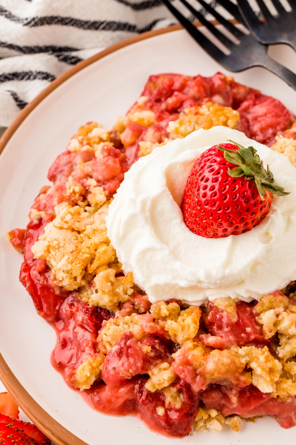 Close-up of Strawberry Dump Cake on a plate with whipped cream and a strawberry on top. 