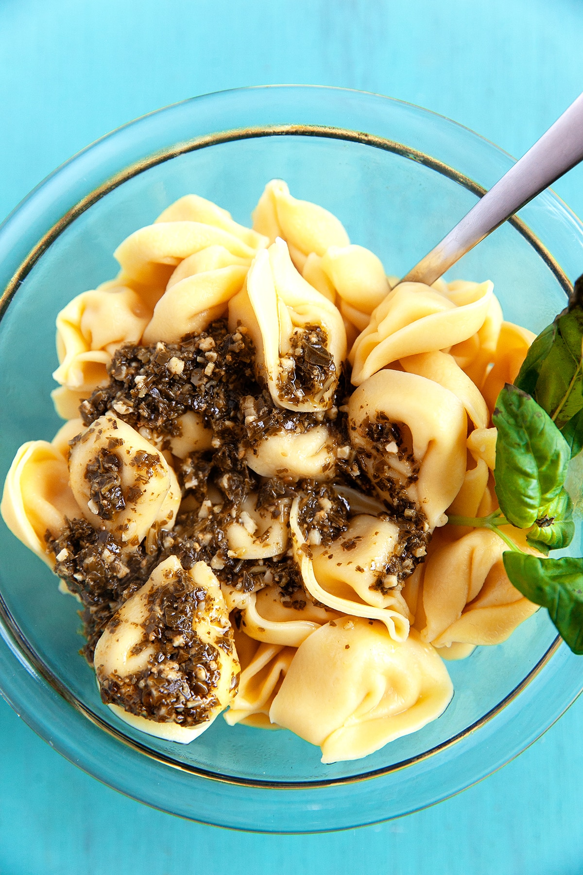 Tortellini being mixed with pesto. 