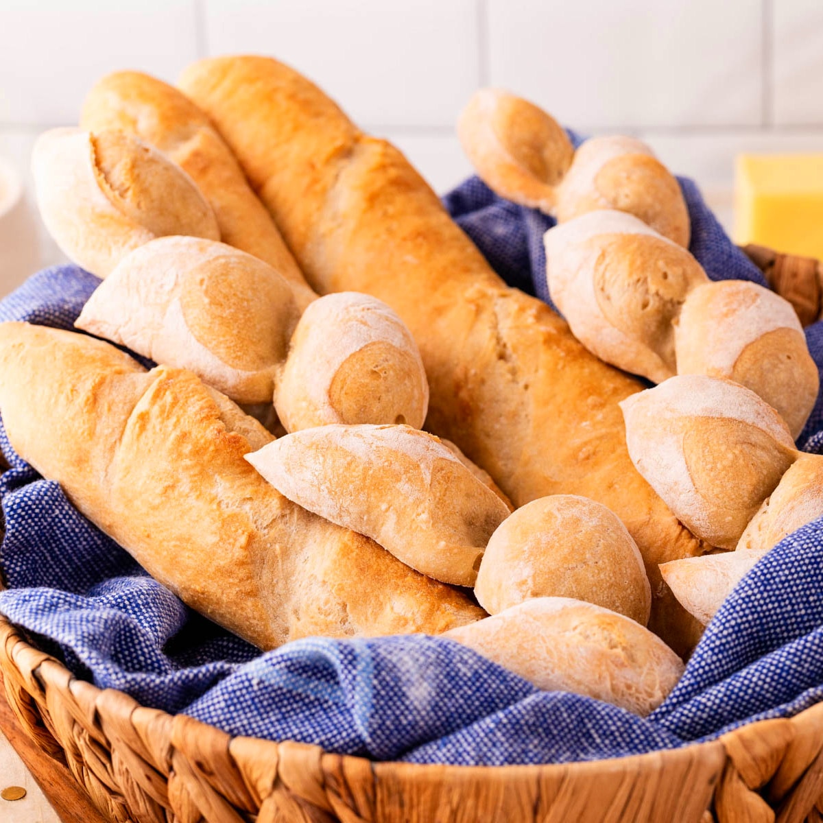 Square photo of baguettes in a basket with a blue tea towel. 