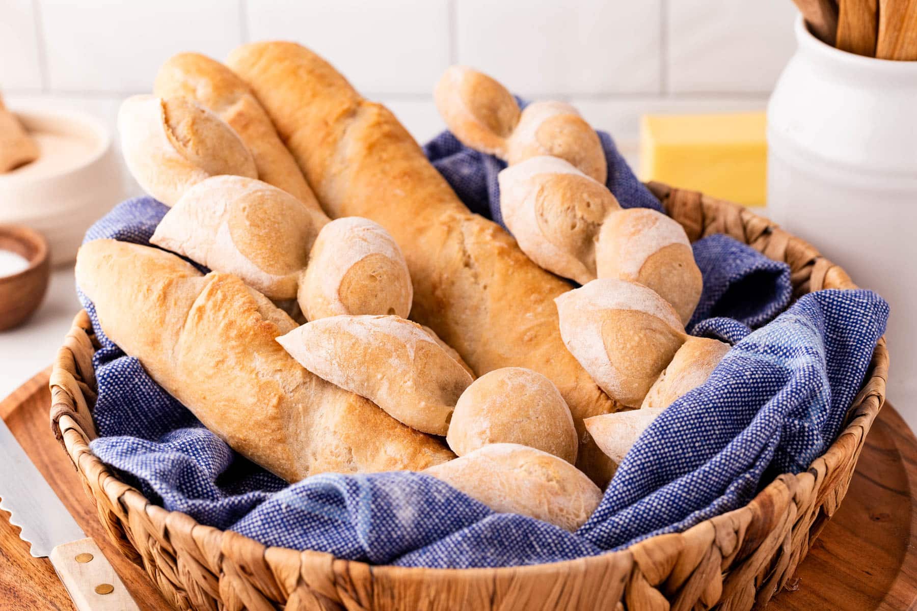 Horizontal photo of baguettes and epi loaves in a basket with a blue tea towel. 