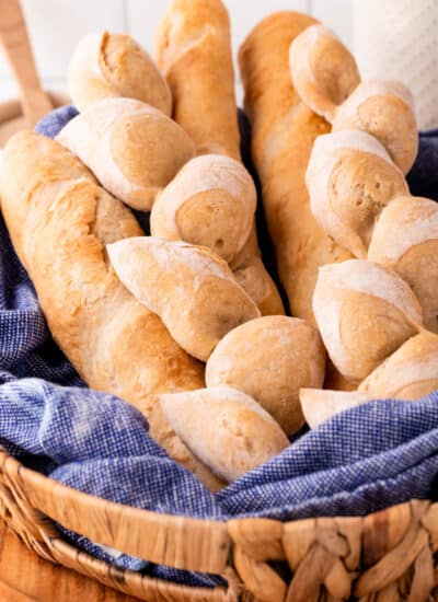 Various French bread in a basket with a blue tea towel.