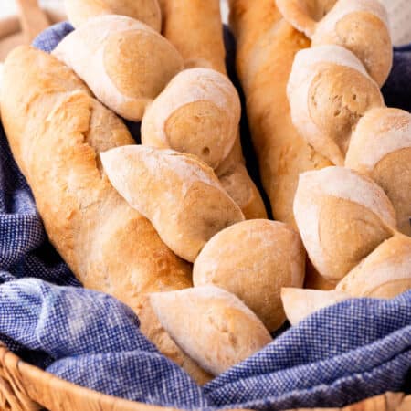 Various French bread in a basket with a blue tea towel.