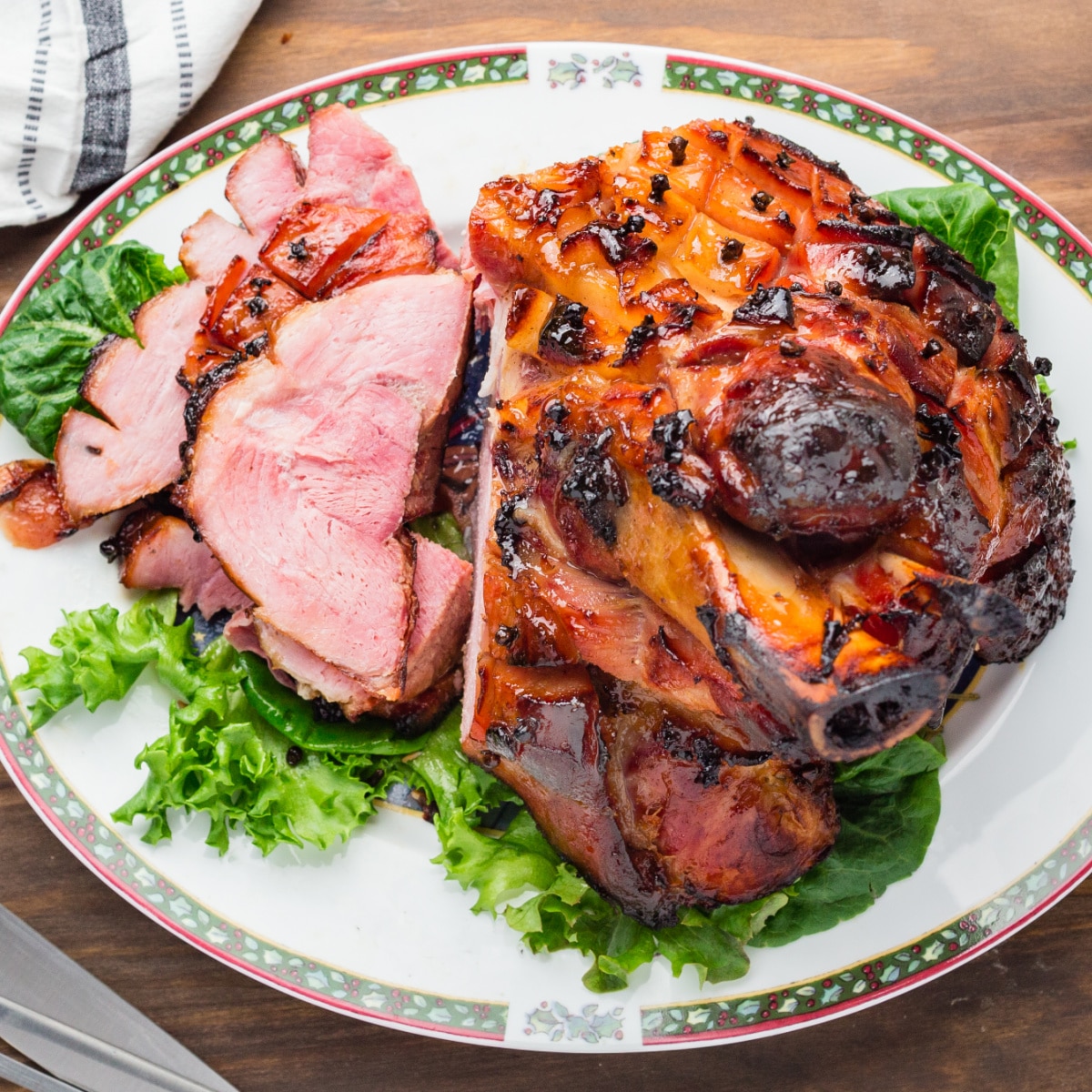 Whole ham with some sliced on lettuce on a platter. 