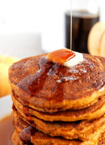 Stacked Pumpkin Pancakes with butter on top and maple syrup pouring on.