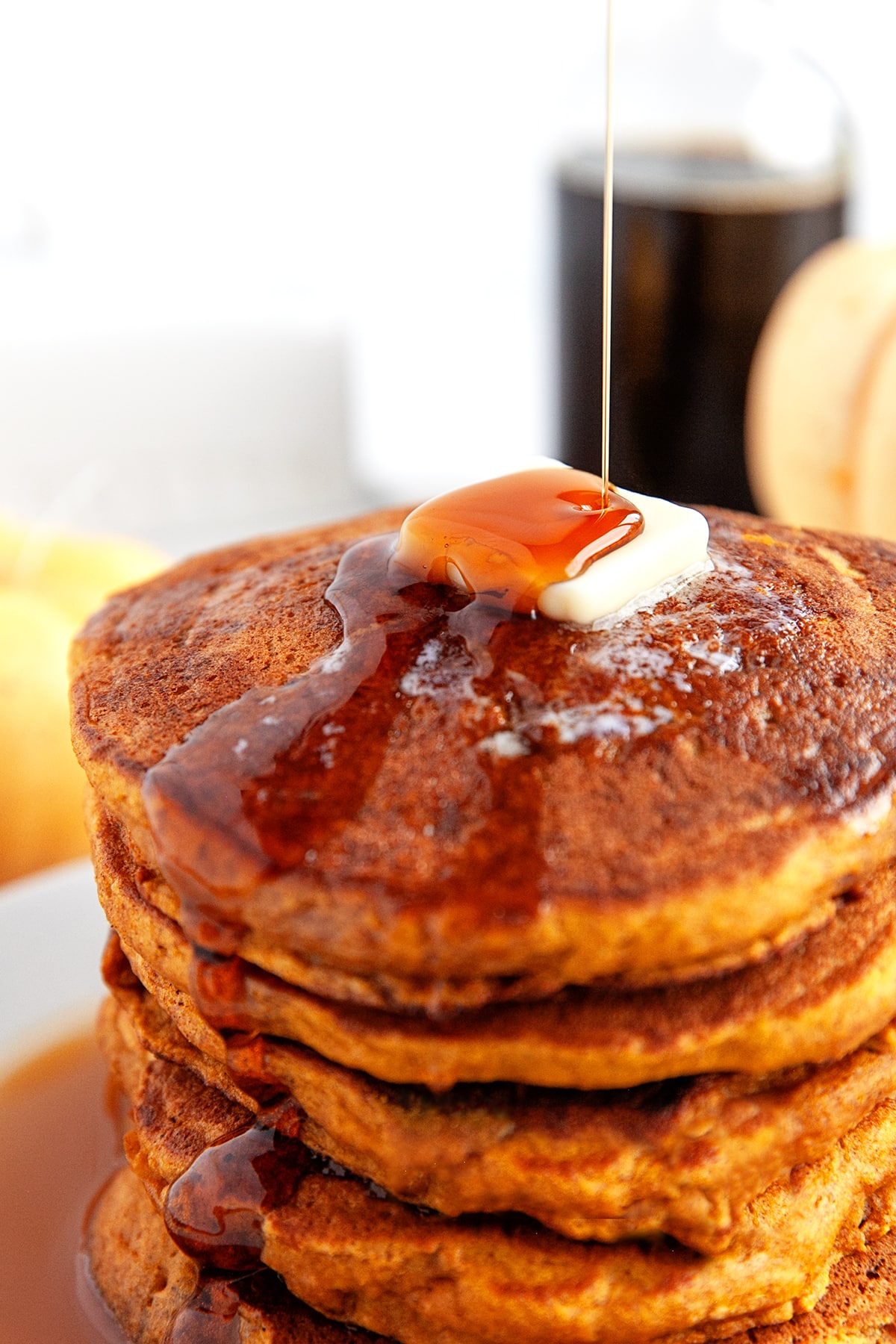 Pouring on maple syrup on a stack of buttered pancakes. 