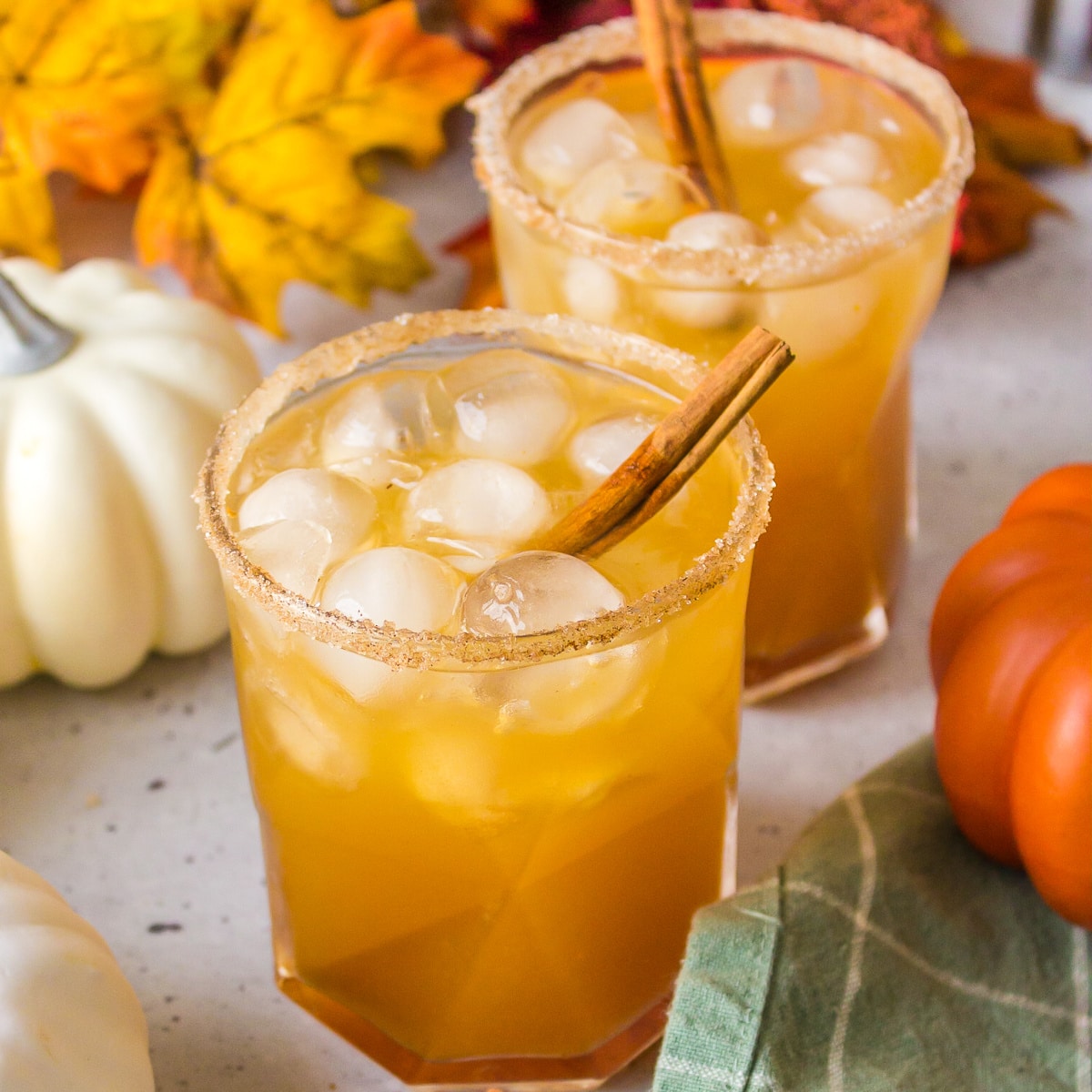Square photo of two cocktails with pumpkins and leaves. 