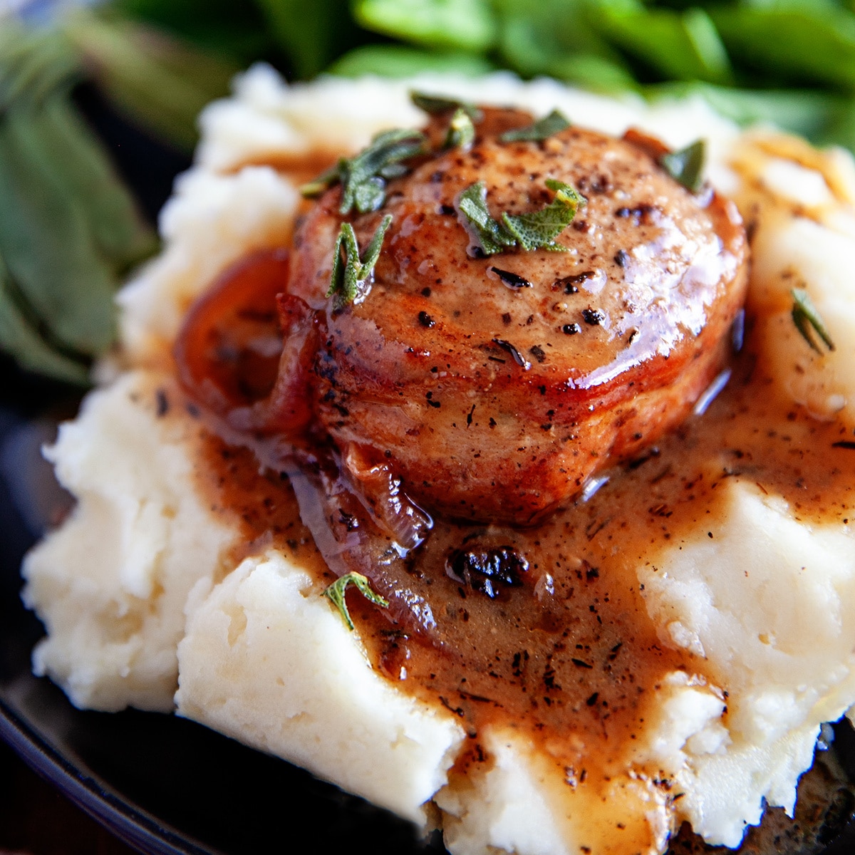 Square photo of a Bacon-Wrapped Pork Tenderloin on mashed potatoes. 