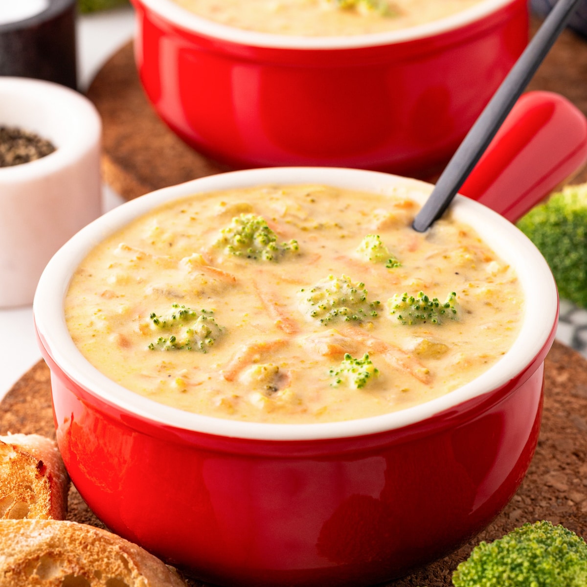 Two red bowls of Instant Pot Broccoli Cheese Soup with black spoons. 