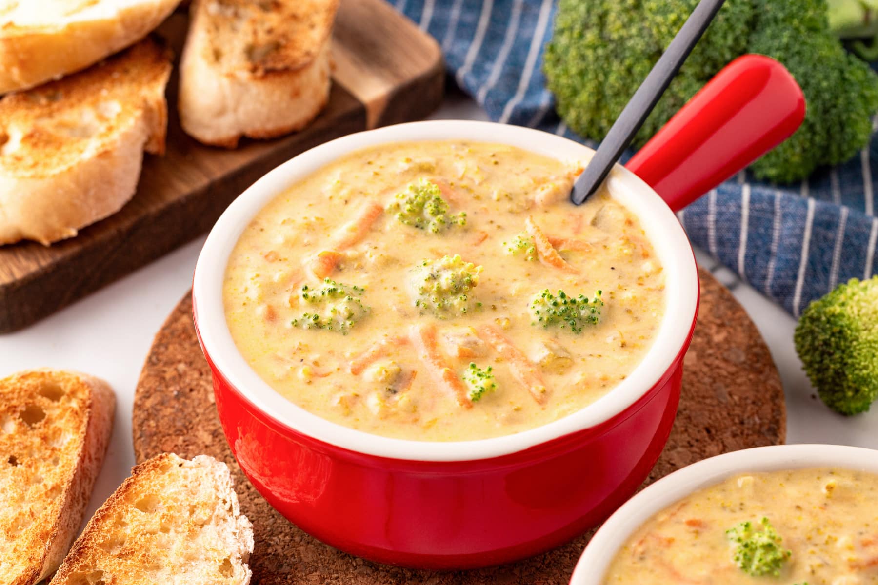 Horizontal picture of broccoli cheese soup in a red bowl with broccoli and toast around it.
