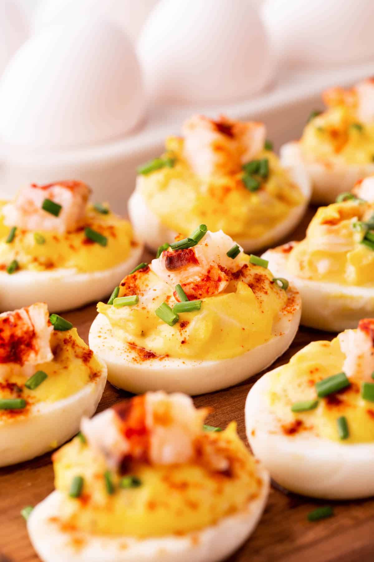 Lobster Deviled Eggs on a board with fresh eggs in the background. 